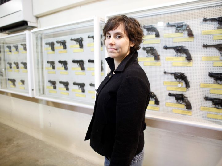 portrait of the artist in front of a case of guns