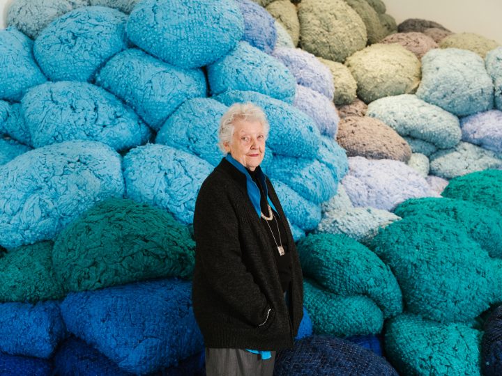 Artist Sheila Hicks stood in front of giant blue balls of thread that form a mountain behind her.