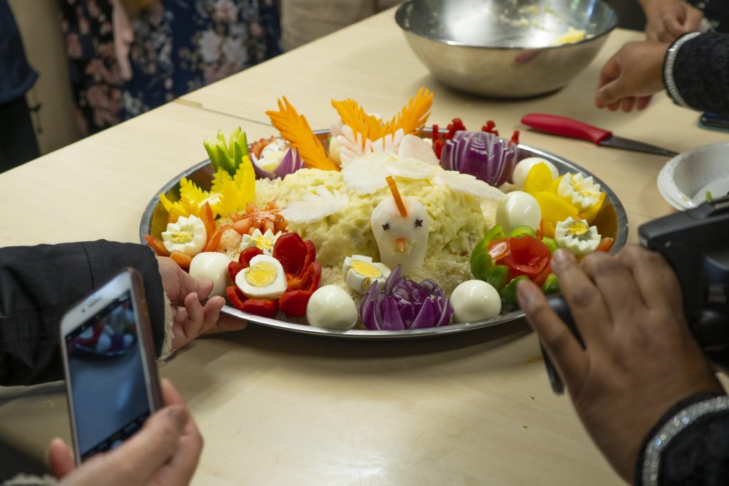 A plate of vegetables and rice designed to look like a chicken, with hands holding phones taking photos.